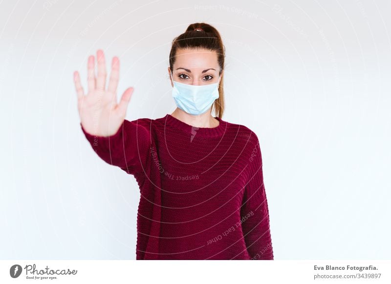 Weiße Frau im Haus, die eine Schutzmaske trägt. Mit der Hand ein Stoppschild machen. coronaviruskonzept covid-19 Coronavirus schützend Mundschutz