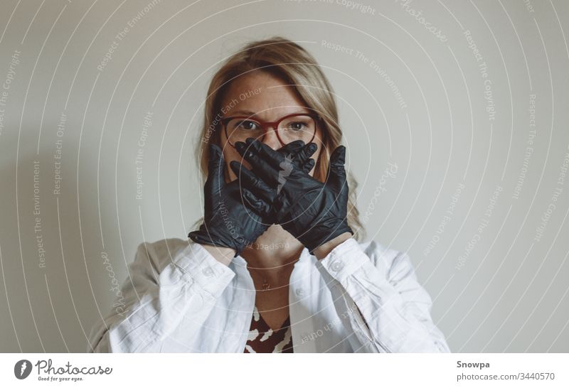 Frau, die ihr Gesicht mit schwarzen Handschuhen bedeckt schwarze Handschuhe Gummihandschuh Arzt Wissenschaftler blond blondes Haar bürsten covid-19 Coronavirus