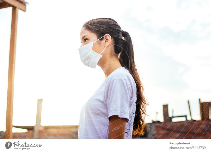 Junge Frau mit einer Maske zum Schutz vor dem Coronavirus COVID-19 an einem sonnigen Tag jung Mundschutz Infektion Seuche covid-19 Erwachsener Krankheit Gesicht