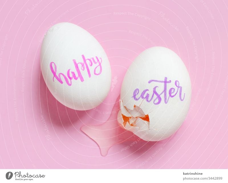 Gebrochene Eier mit handschriftlicher Aufschrift HAPPY EASTER über rosa Hintergrund Ostern Glück frohe Ostern gebrochen zerbrochenes Ei Draufsicht Konzept
