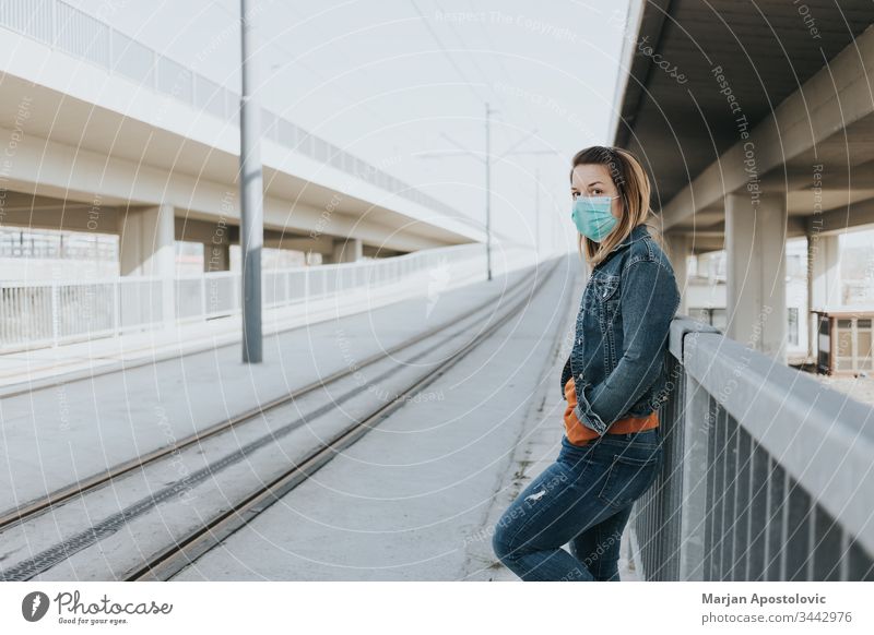 Junge Frau mit einer chirurgischen Maske in einer leeren Straßenbahnhaltestelle allein Biogefährdung Pflege Kaukasier Großstadt Ansteckung Coronavirus covid-19