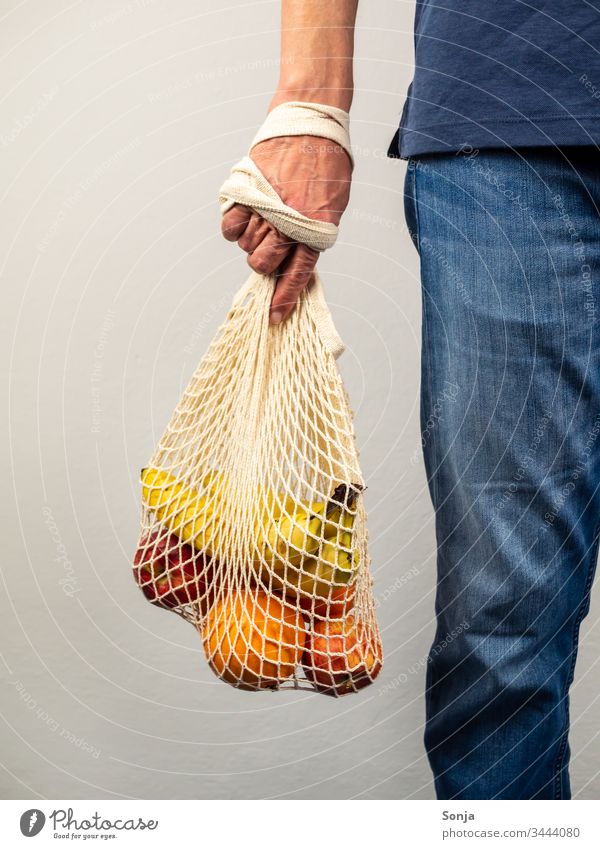Mann hält wiederverwendbare Tasche mit frischem Obst in seiner Hand, gesunde Ernärhung, plastikfrei einkaufen Frucht Banane orange apfel Vitamin