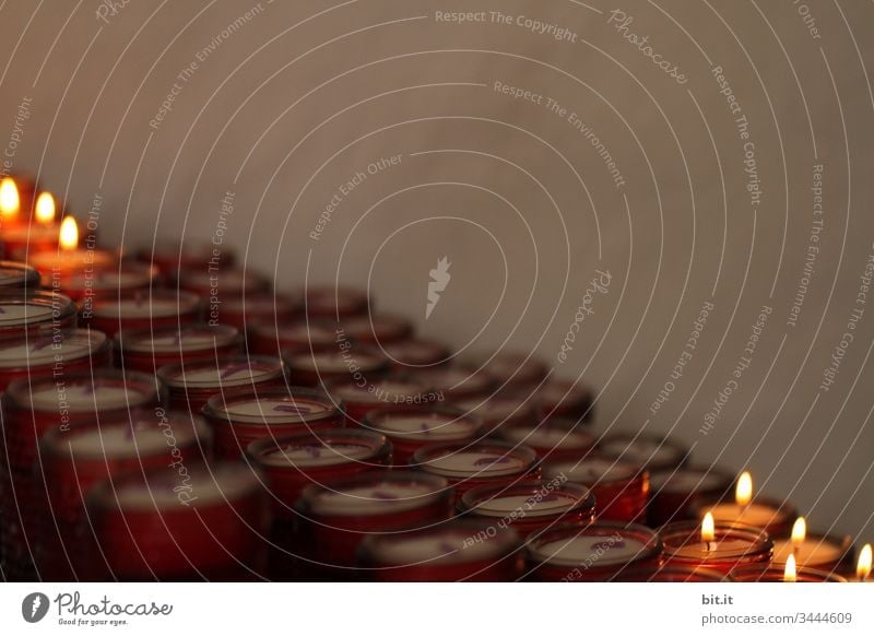 Brennende, leuchtende Kerzen in einem Opferstock in der Kirche, vor einer grauen Wand in trauriger Stimmung. Schwache Tiefenschärfe Lichterscheinung