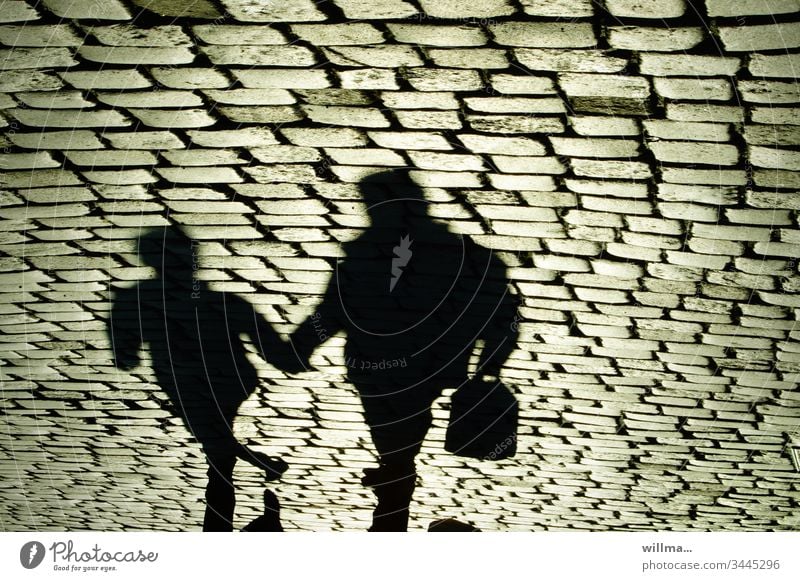 Schatten von zwei Personen auf dem Kopfsteinpflaster Einkaufsbummel Stadtbummel Mensch Pflastersteine Menschen Hand in Hand Zusammensein Vater und Kind