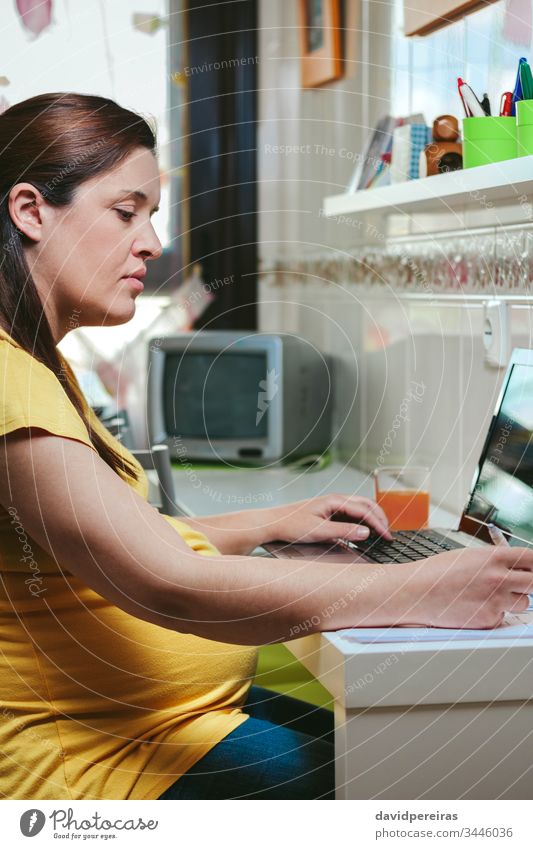 Frau, die von zu Hause aus mit einem Laptop arbeitet schwanger von zu Hause aus arbeiten Coronavirus Seuche Einsperrung Risikogruppe zu Hause bleiben Küche
