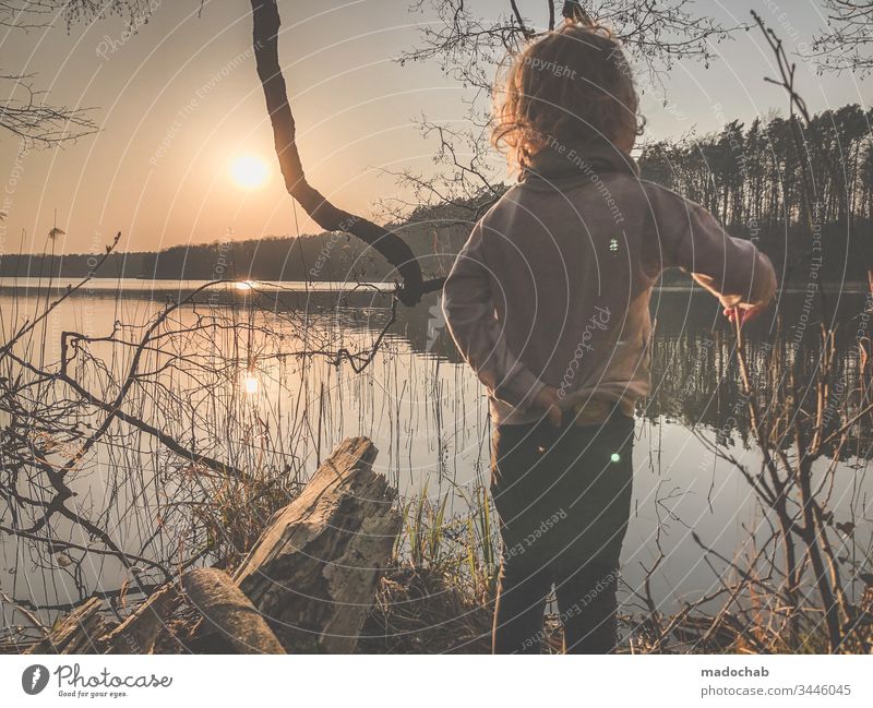 Kind steht beim Sonnenuntergang am Seeufer und blickt in die Zukunft Wasser sonne Natur Wald Junge Sonnenlicht Gegenlicht romantidch Dämmerung Landschaft Umwelt