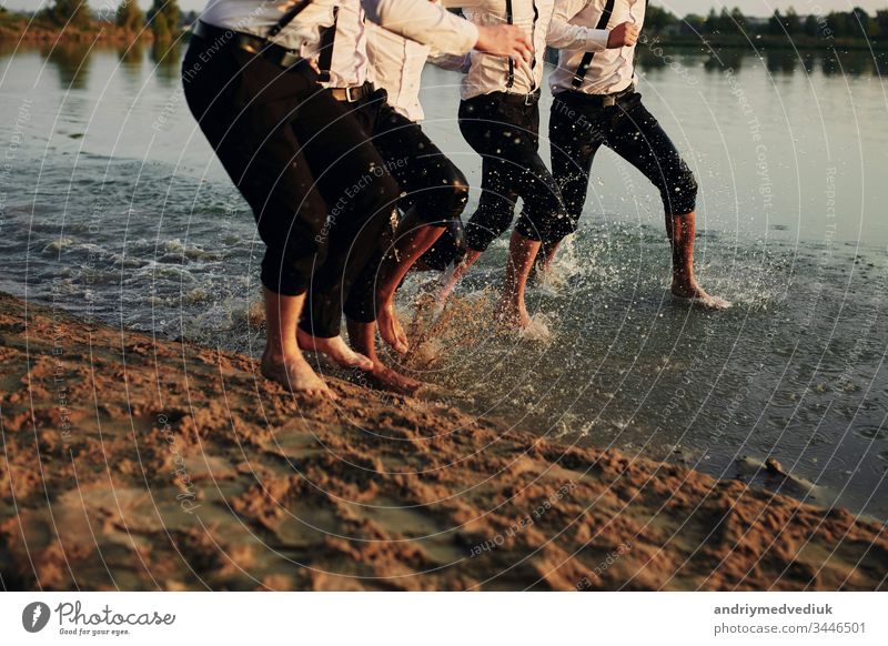 Männerfüße im Wasser. Männer in Kostümen laufen auf dem Wasser. Sie haben Spaß, spielen und spritzen Wasser um sich herum. Sommer. Gruppe glücklicher junger Männerfüße spritzen Wasser im Meer und spritzen am Strand