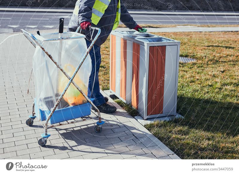 Reinigungskraft beim Ausleeren des Mülls. Mann mit gelber Weste, der einen Behälter reinigt, steht neben einem Reinigungswagen. Echte Menschen, authentische Situationen