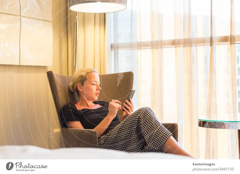 Geschäftsfrau auf Geschäftsreise, müde von einem Geschäftstermin, sitzt nach der Arbeit allein im Hotelzimmer, liest und beantwortet E-Mails und Nachrichten auf ihrem Smartphone