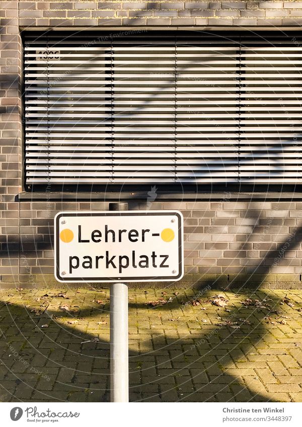 Leerer Parkplatz. Ein Schild 'Lehrerparkplatz' vor einem Schulgebäude mit geschlossenen Rollläden Hinweisschild Schilder & Markierungen Schriftzeichen