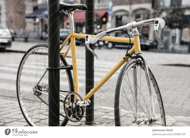 Gelbes Vintage-Rennrad mit Bügelschloss an Straßenschild angeschlossen Fahrrad Retro Tour de France Chrom Stahlrohl Pedale Kette Ritzel Rad Reifen Mantel Bremse