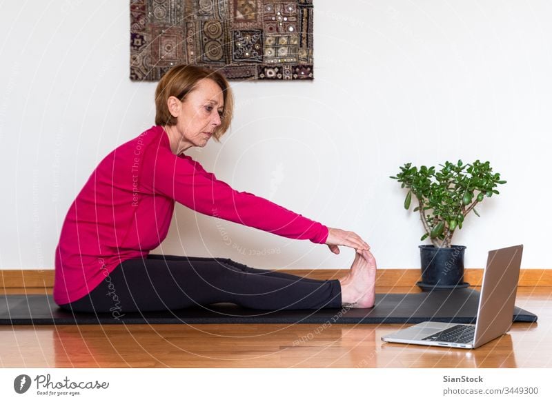 Frau mittleren Alters sieht sich auf ihrem Laptop ein Online-Video-Tutorial mit Yoga-Übungen an. Konzept Yoga zu Hause. Biegen Schönheit Training Europäer