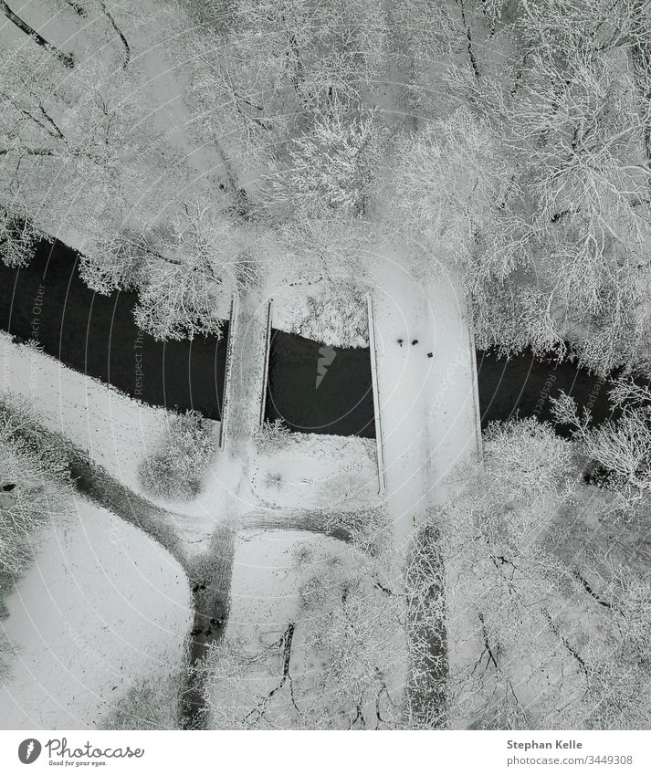 Eine schneebedeckte Brücke, auf der Menschen hoch oben in einer kalten Winterlandschaft spazieren gehen. Schnee laufen vertikal Dröhnen Antenne Baum Fluss