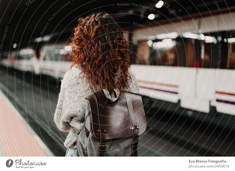 junge, schöne Frau am Bahnhof mit dem Handy, bevor sie den Zug erreicht. Ansicht von hinten. Reise-, Technologie- und Lifestyle-Konzept reisen Station bewegend