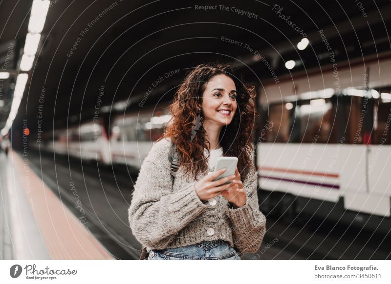 junge, schöne Frau am Bahnhof mit dem Handy, bevor sie den Zug erreicht. Ansicht von hinten. Reise-, Technologie- und Lifestyle-Konzept reisen Station bewegend