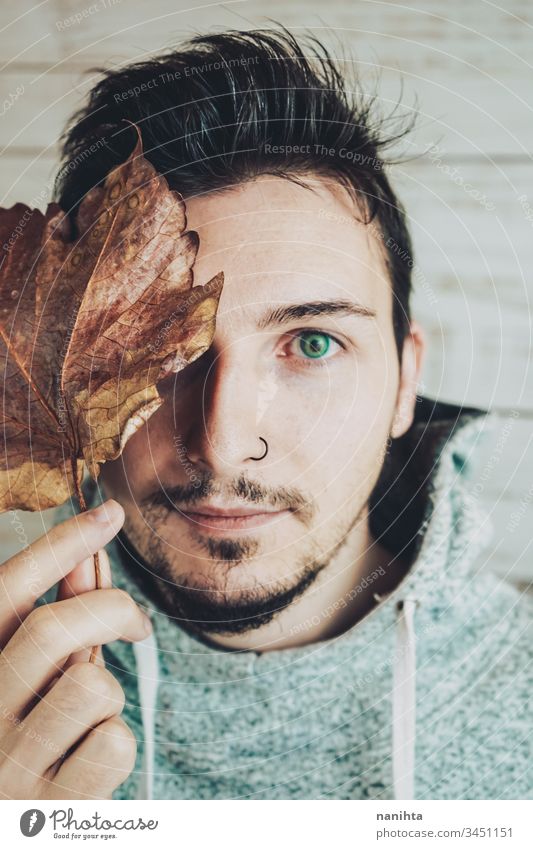 Junger Mann bedeckt sein Gesicht mit einem trockenen Blatt attraktiv cool männlich Porträt Herbst kreativ künstlerisch Vollbart Piercing Nase schließen