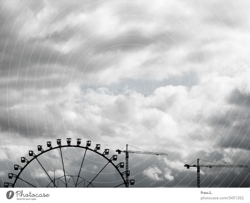 Die stillgestellten Käne, das geschlossene Riesenrad, auch der aufgeplusterte Himmel fühlten sich irgendwie indifferent. Kräne Rummel Menschenleer Wolken