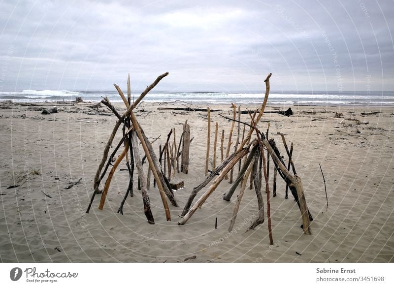Holzzelt an einem Strand in Oregon hölzern Zelt Sand Meer Wasser grau raues Wetter reisen schön Urlaub Wellen Stöcke selbst gemacht Haus Hütte wood wooden