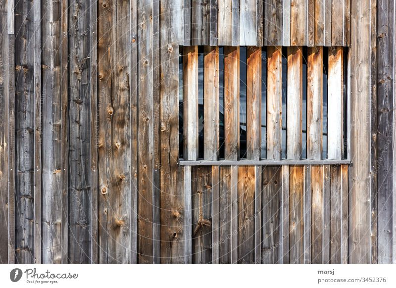 Holzwand mit einem Fenster, das mit Kanthölzern verbarrikadiert ist. braun Holzmaserung Wand Rechteck rechteckig geometrisch verwittert raue Kanten