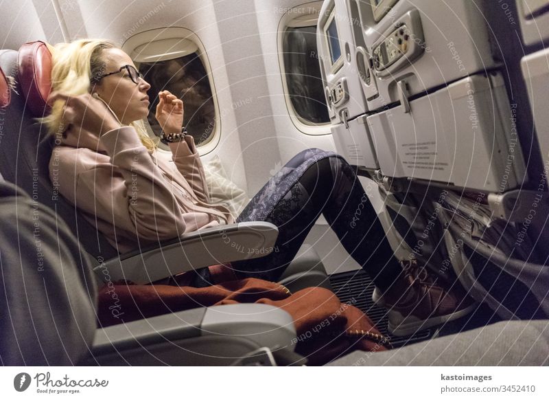 Sportlich-lässige junge blonde kaukasische Dame, die während einer Flugreise durch das Fenster einen Film sieht. Kommerzieller Transport in Flugzeugen