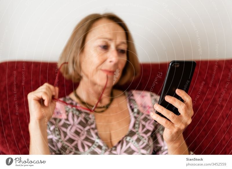 Elegante, reife Frau, die ein Smartphone benutzt, während sie auf dem Sofa sitzt virtuell einkaufen Lifestyle-Elektronik Gespräch Halt hübsch Talkrunde