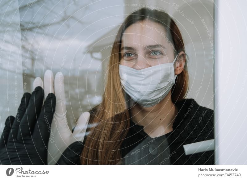 glückliche Frau, die sie gebraten sah und die sie wegen eines Coronavirus covid-19 mit Maske und Handschuhen am Fenster zu Hause besuchte soziale Distanzierung