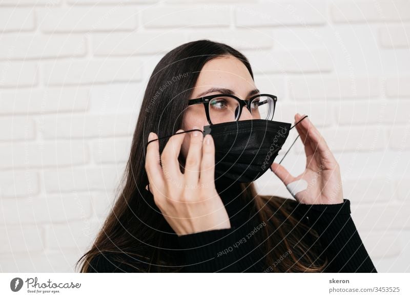 Das brünette Mädchen mit Brille zur Sehkorrektur ist vor einer Virusinfektion geschützt: dem Coronavirus. Eine Frau mit schwarzer medizinischer Maske während der Pandemie 2019-nCoV COVID. der Patient in Quarantäne