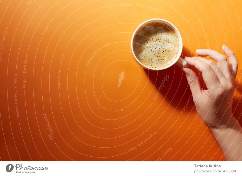Eine Tasse schwarzer Kaffee mit einer weiblichen Hand auf einem leuchtend orangefarbenen Hintergrund. Minimalismus, Draufsicht. copyspace Becher trinken Design