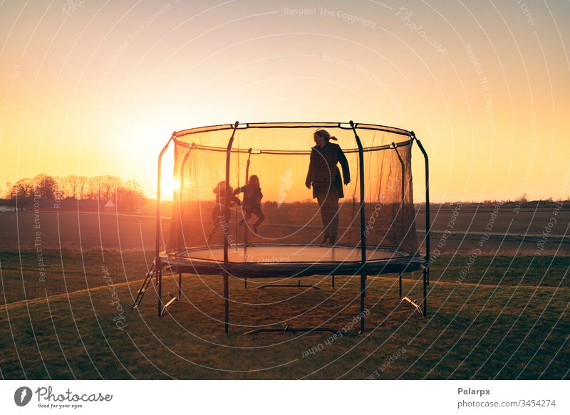 Trampolin auf einer Wiese im Sonnenuntergang mit zwei Kindern Erholung Silhouetten Morgendämmerung Sonnenstrahlen blond Gleichgewicht Aktion Kunstturnen Sport