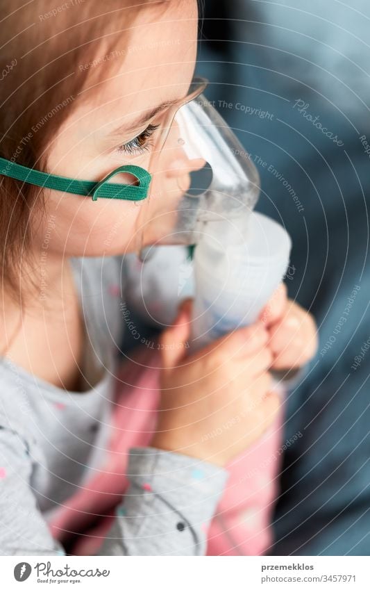 Krankes kleines Mädchen, das eine medizinische Inhalationsbehandlung mit einem Vernebler erhält. Kind mit Atemschutzmaske auf dem Gesicht sitzend im Bett Virus