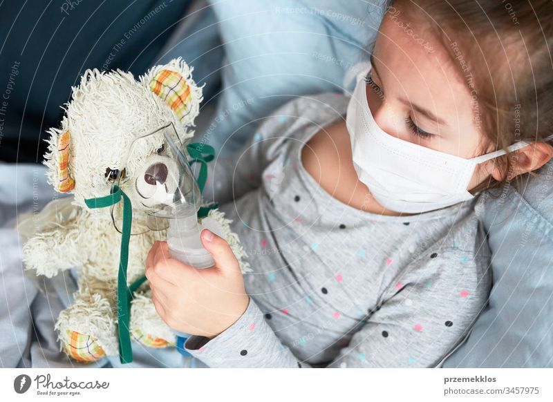 Krankes Kind erholt sich im Bett. Kleines Mädchen spielt, indem es eine medizinische Inhalationsbehandlung mit einem Vernebler an ihrem Teddybär vornimmt. Virus