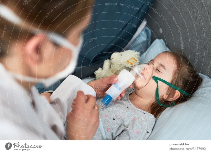 Der Arzt besucht den kleinen Patienten zu Hause. Kind, das eine medizinische Inhalationsbehandlung mit einem Vernebler erhält. Mädchen mit Atemmaske im Gesicht. Frau mit Uniform und Gesichtsmaske.