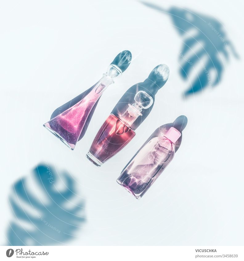 Rosa Kosmetikproduktflaschen im Sonnenlicht auf weißem Hintergrund mit tropischen Monsterblättern im Schatten. Ansicht von oben. Moderne Hautpflege. Parfüms. Flach liegend. Durchsichtig. Schönheitskonzept