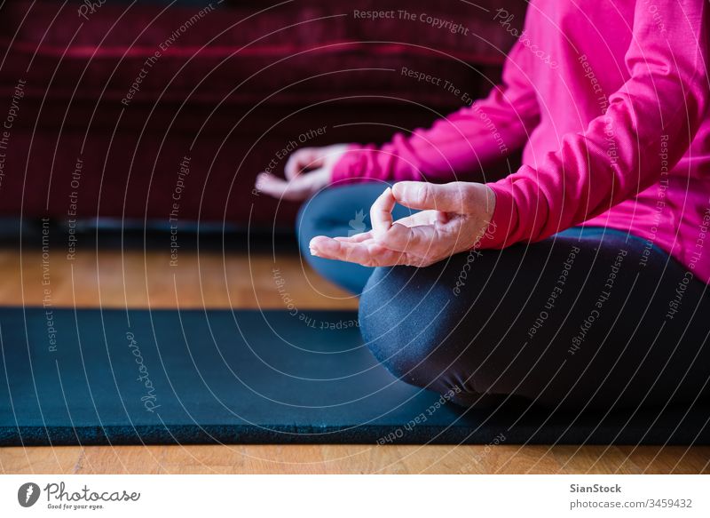 Nahaufnahme der Hände einer Frau mittleren Alters, die in Lotusstellung auf einer Yogamatte in ihrem Wohnzimmer sitzt. Biegen Schönheit Training Europäer
