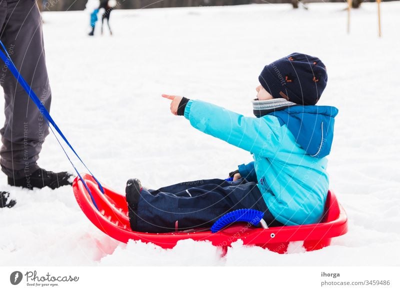 Junge mit rotem Schlitten im Schnee Winter aktiv Kind Kindheit kalt Spaß lustig Fröhlichkeit Glück Hut Feiertag Kinder gestrickt Freizeit wenig Berge u. Gebirge