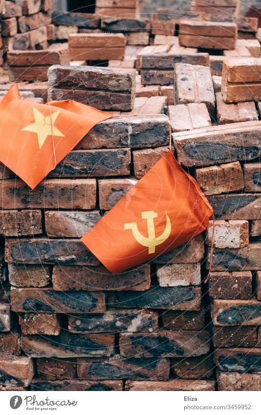 Die vietnamesische Flagge neben einer Fahne mit Hammer und Sichel, was den kommunistischen Staat symbolisiert, vor einem Haufen mit roten Ziegelsteinen