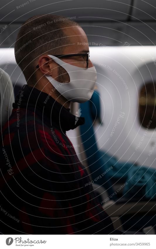Mann sitzt während der Corona Pandemie mit Gesichtsmaske im Flugzeug Maske Stoffmaske Coronavirus Prävention Virus Mundschutz COVID Infektionsgefahr Gesundheit