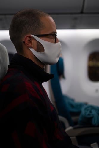 Mann sitzt während der Corona Pandemie mit Gesichtsmaske im Flugzeug Maske Stoffmaske Coronavirus Prävention Virus Mundschutz COVID Infektionsgefahr Gesundheit