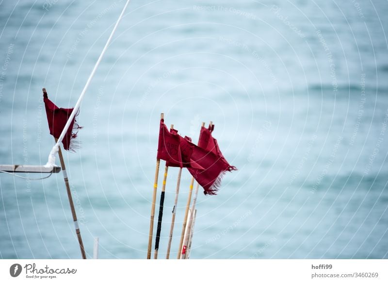 rote Fahnen im Wind auf Fischerboot Rote Fahne Fahnenmast maritim wild windig Meer auf see wehen Himmel flattern blau Sommer
