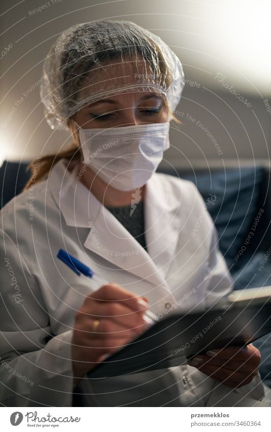Arzt, der ein Dokument ausfüllt. Krankenhauspersonal arbeitet im Nachtdienst. Frau trägt Uniform, Mütze und Gesichtsmaske, um eine Virusinfektion zu verhindern.