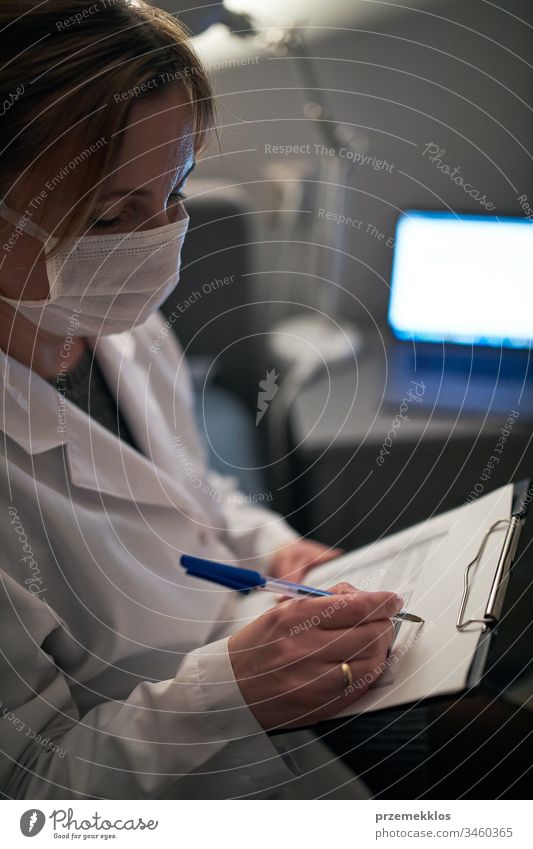 Arzt, der ein Dokument ausfüllt. Krankenhauspersonal arbeitet im Nachtdienst. Frau trägt Uniform, Mütze und Gesichtsmaske, um eine Virusinfektion zu verhindern.
