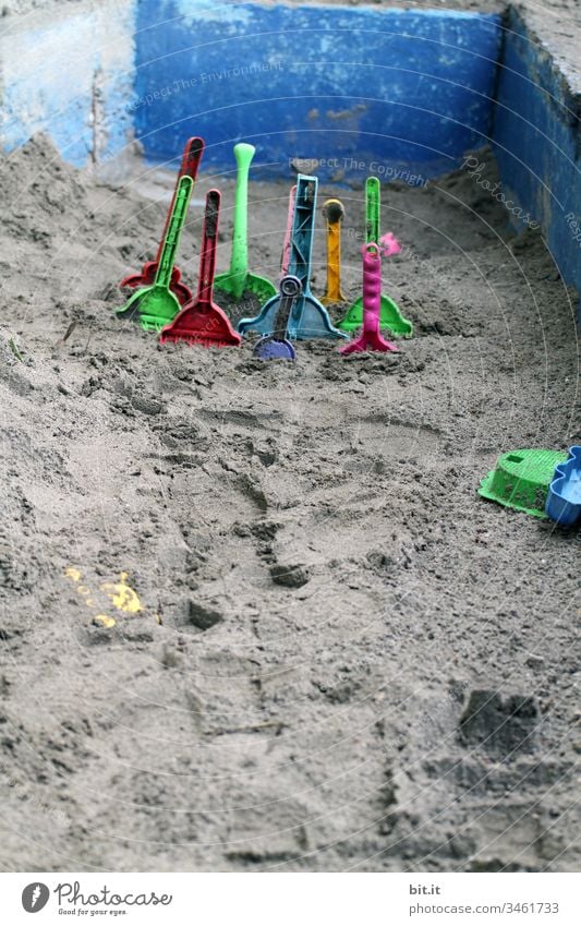 Viele, bunte Sandschaufeln aus Plastik stecken im Sand, in einem leeren Sandkasten aus Stein, im Urlaub. Sandelschaufel Schaufel Spielen Spielzeug Kindheit