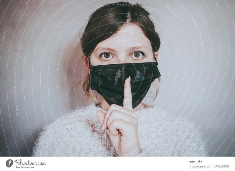 Junge Frau, die eine Gesichtsmaske trägt und um Schweigen bittet Bund 19 COVID Coronavirus Virus Atem Pandemie Mundschutz Stille geheim Lügen Windstille Geduld