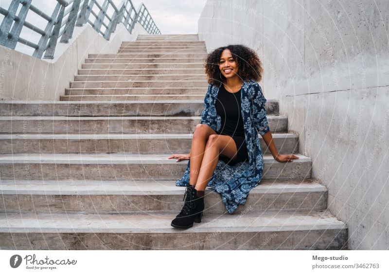 Afroamerikanische Frau, die auf Stufen sitzt. Afro-Look grau jung Mädchen Gesicht Wand Ausdruck Erwachsener Blick Mode schwarz Stehen Lächeln selbstbewusst
