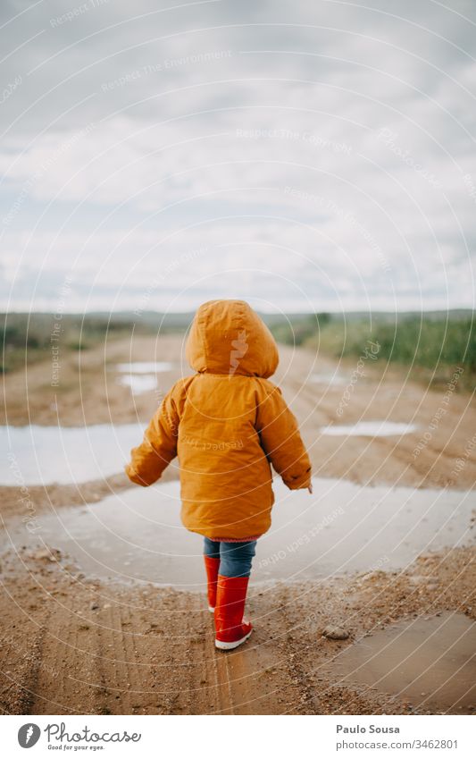 Rückansicht eines in einer Pfütze laufenden Kindes mit orangefarbener Jacke Gummistiefel rot nass Außenaufnahme Farbfoto Regen Mensch Freude Wasser Spielen