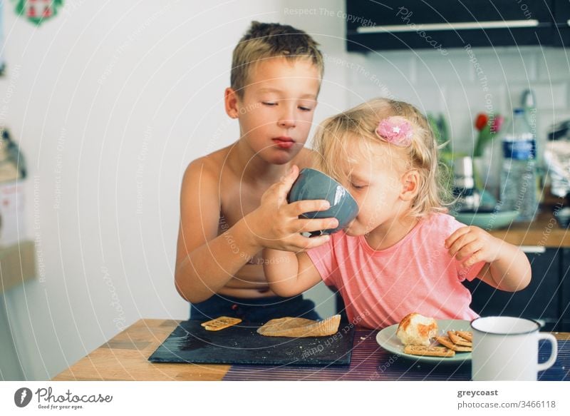 Älterer Bruder und kleine Schwester beim Frühstück in der Küche. Vorsichtig Junge hilft Mädchen trinken aus der Tasse Kinder Morgen Pflege Tee Mahlzeit