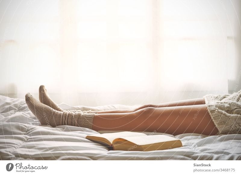 Weiches Foto von Frauenbeinen auf dem Bett mit einem alten Buch neben ihr lesen Fenster Ansicht LAZY Sonntag Winter Kaffee Tasse Tee Morgen Mädchen heimwärts