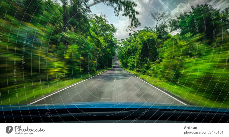 Blick von vorne auf blaues Auto auf Asphaltstraße und Geschwindigkeitsunschärfe auf Autobahn im Sommer mit grünen Bäumen Wald auf dem Land abstrakt Kunst