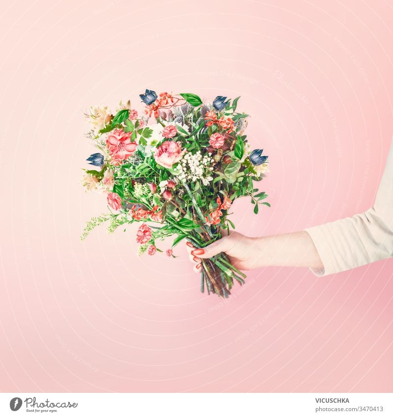 Weibliche Hand hält hübsches Blumenstrauß-Arrangement mit verschiedenen Blumen und Blättern auf blassrosa Hintergrund. Floristin mit Blumenstrauß. Begrüßung. Muttertag .