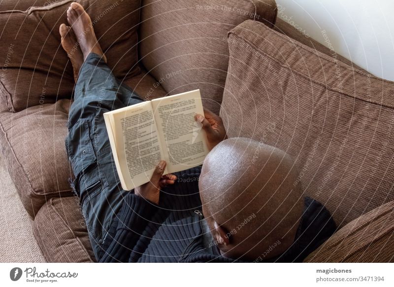 Schwarzer Mann, afrikanischer Ethnie, liest auf dem Sofa 40s Karibik Erwachsener Afrikanisch Amerikaner schwarz Buch Briten lässig Komfort bequem Konzept Liege